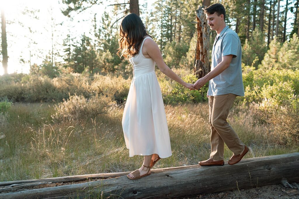 engaged couple playing on fallen log in lake tahoe meadow