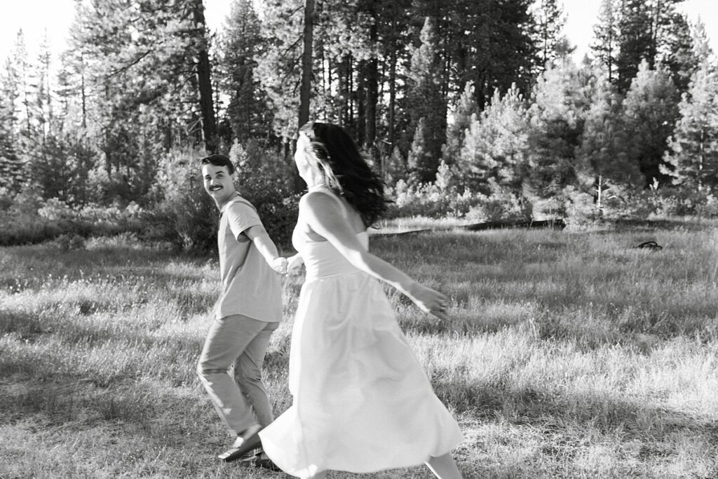 couple runs joyfully through a lake tahoe meadow at zephyr cove