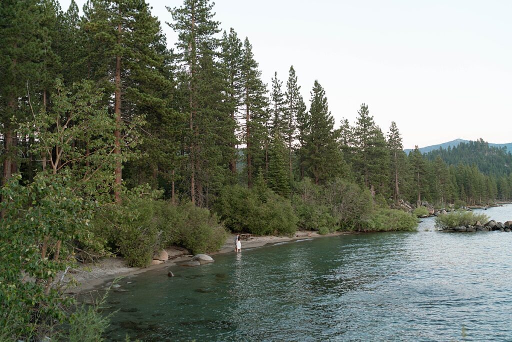 couple walking at the beach in lake tahoe from a distance captured by reno tahoe engagement photographer