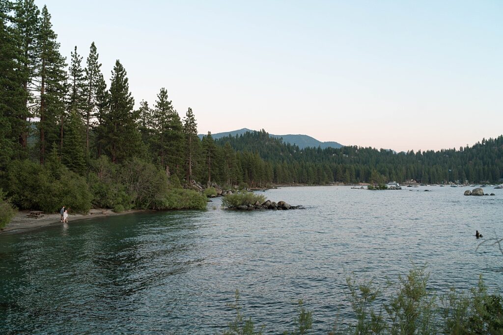 couple walking at the beach in lake tahoe from a distance captured by reno tahoe engagement photographer