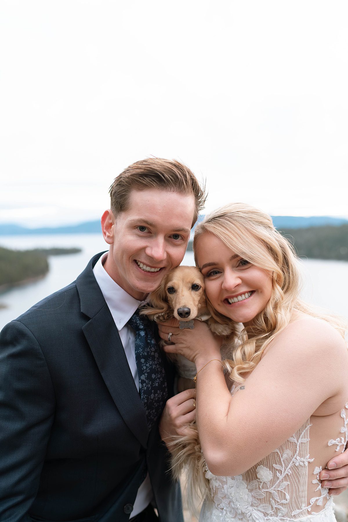 Couple's portrait holding their puppy. Sunrise Elopement ceremony at Emerald Bay captured by Lake Tahoe Wedding Photographer