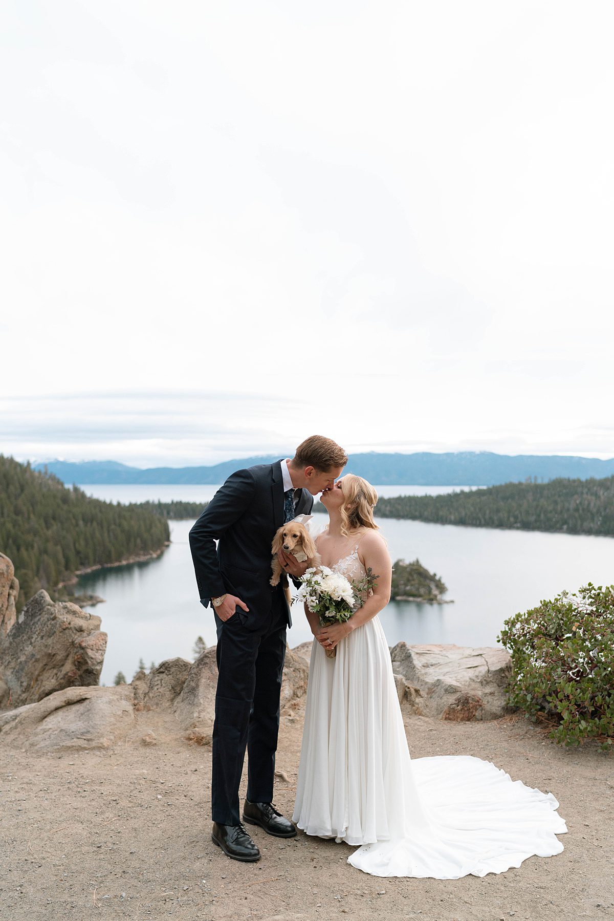 Couple's portrait holding their puppy. Sunrise Elopement ceremony at Emerald Bay captured by Lake Tahoe Wedding Photographer